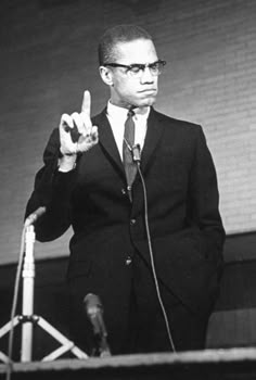 a man in a suit and tie making the peace sign with his hand while standing behind a microphone