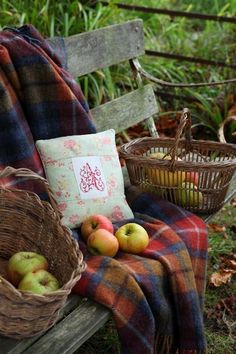 an old wooden bench with apples in baskets on it and a plaid blanket draped over it