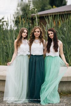 three young women standing next to each other in long green skirts and white tops, posing for the camera