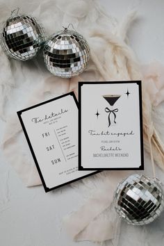 two silver disco balls are next to some black and white wedding stationery on a table