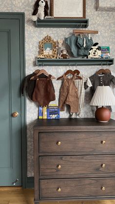 a dresser with two baby clothes on top of it next to a blue door and wallpaper