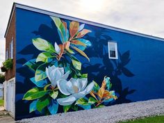 a painted mural on the side of a blue building with white flowers and green leaves