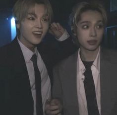 two young men in suits and ties posing for the camera at an event with one holding his hand up to his ear