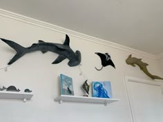 three shark sculptures are on the wall above two floating shelfs with pictures and paintings