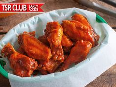 a green bowl filled with chicken wings on top of a wooden table