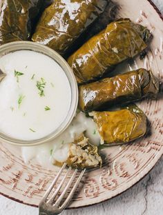 stuffed grape leaves with yogurt in a bowl on a plate next to a fork