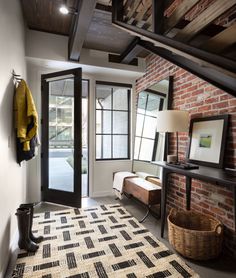 a room with brick walls and black doors, a rug on the floor and a coat rack