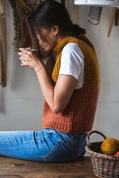 a woman sitting on the floor next to a basket with yarn in it and knitting