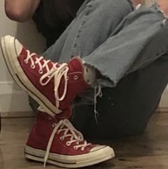 a woman sitting on the floor with her legs crossed and wearing red converses,