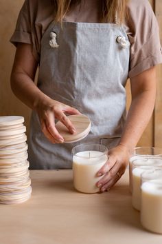 a woman in an apron is decorating some plates with candles and jars on the table