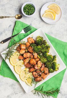 a white plate topped with chicken and broccoli next to lemon wedges on a green napkin