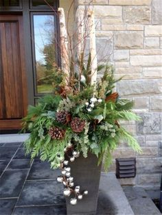 a tall planter filled with lots of greenery and pine cones on top of a stone walkway