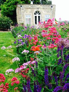 colorful flowers in front of an old stone building and green grass area with red, pink, purple, and white flowers