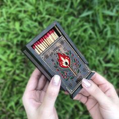 a person holding an open matchbox with matches in it on top of green grass