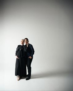 two people are posing for the camera in front of a white background and one is wearing a black dress