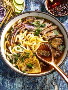 a bowl filled with noodles, meat and vegetables on top of a blue wooden table