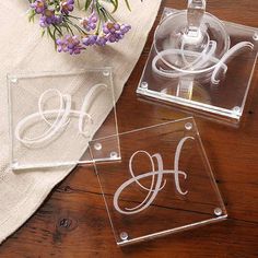 two clear acrylic coasters sitting on top of a wooden table next to purple flowers