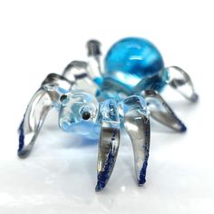 a blue glass crab sitting on top of a white table next to two silver claws