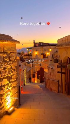 an alley way leading to some buildings with lanterns in the sky above it at sunset