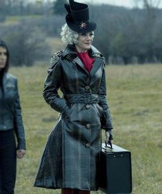 a woman in a hat and trench coat holding a suitcase while standing next to another woman