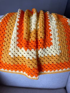 an orange and white crocheted blanket sitting on top of a blue couch next to a pillow