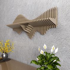 a vase with flowers on a table next to a wooden wall sculpture and potted plant