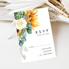 a white wedding card with sunflowers and greenery on the front is sitting next to some feathers