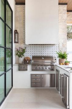 an outdoor kitchen with stainless steel appliances and white counter tops, along with potted plants