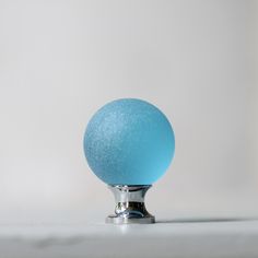 a blue ball sitting on top of a metal stand in front of a white wall