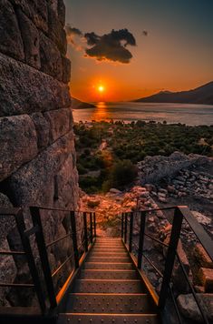 the sun is setting over some rocks with stairs going up to it and there are trees in the foreground