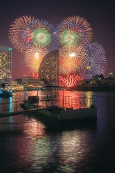 fireworks are lit up in the night sky over water and city buildings with lights on them