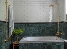 a bathroom with green marble tile and gold faucet, bathtub, shower head, and towel rack