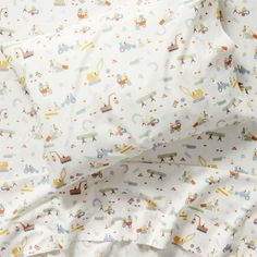 a close up view of a bed with white sheets and colorful transportation print on it