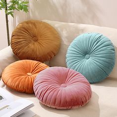 four different colored pillows sitting on top of a couch next to a potted plant