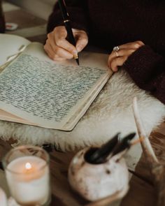 a woman is writing on an open book with a pen in her hand while sitting at a table