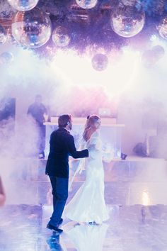 a bride and groom are dancing on the dance floor with bubbles in the air behind them