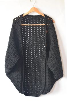 a black sweater hanging up on a white wall with a wooden hanger holding it