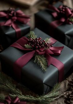 three presents wrapped in black paper and tied with red ribbon, sitting next to pine cones