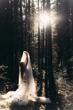 a woman in a wedding dress standing in the woods with her arms behind her back