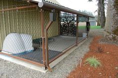 a dog kennel in the middle of a gravel area with trees and grass behind it