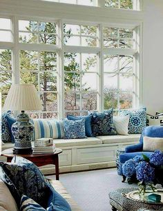 a living room filled with blue and white furniture next to a large window covered in lots of windows