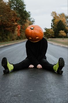 a person sitting in the middle of an empty road with a pumpkin on their head