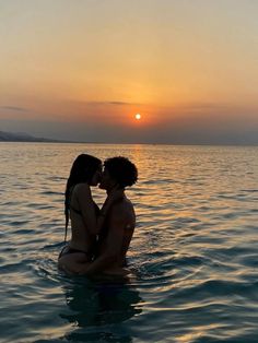 two people are sitting in the water at sunset, one is kissing the other's forehead