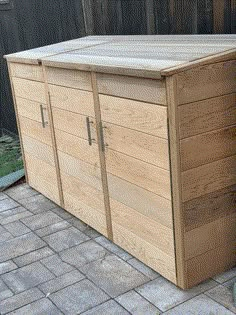 a large wooden storage box sitting on top of a brick patio next to a fence