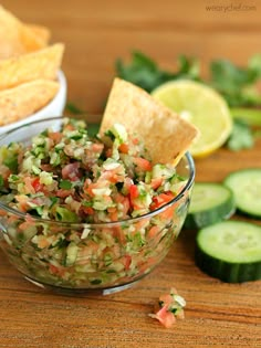 a bowl filled with guacamole and tortilla chips next to sliced cucumbers