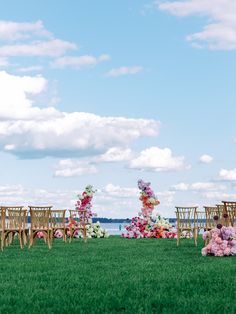 an outdoor ceremony set up with chairs and flowers on the grass by the water's edge