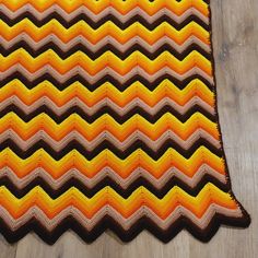 an orange and brown crocheted blanket on a wooden floor