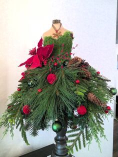 a dress made out of pine cones and red poinsettis sits on a mannequin