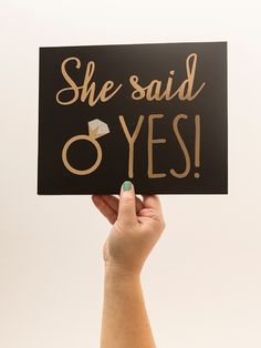 a woman holding up a sign that says she said yes with gold lettering on it