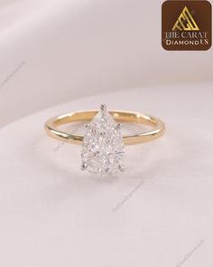 a yellow gold engagement ring with a pear shaped diamond in the center, on a white background